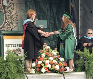 a graduate in green robes receiving a high school diploma